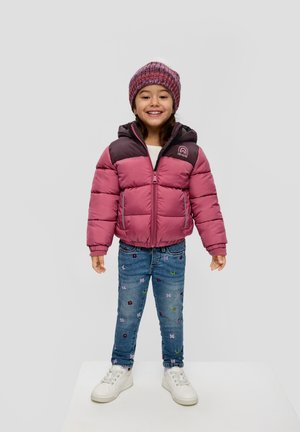 Roze en donkerjack met capuchon, met een gewatteerd ontwerp. Blauwe jeans versierd met bloemenpatronen. Witte sneakers. Glimlachend kind.