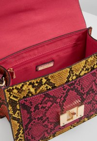 Sac à main avec motif en peau de serpent jaune et rose, fermoir doré et dessus ouvert montrant l'intérieur en tissu rouge avec poche zippée.