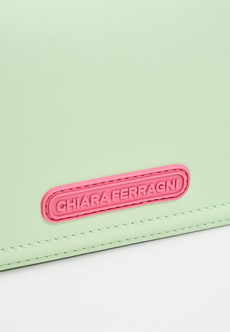 Cartera verde de cuero sintético con superficie texturizada, parche del logo en rosa y costuras en contraste a lo largo de los bordes.