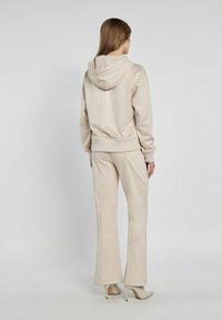 Beżowy, welurowy hoodie z kapturem i ściągaczami, w zestawie z pasującymi spodniami dzwonami. Gładka tekstura i minimalistyczny design.