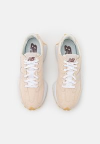 Paire de baskets beige New Balance avec lacets blancs et logos marron, positionnées côte à côte sur fond blanc.