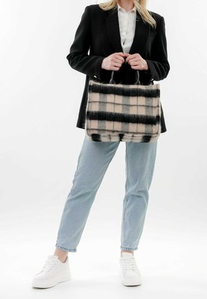 Kvinde iført sort blazer, hvid skjorte, lyseblå jeans, hvide sneakers, der holder en stor, blød, beige og sort ternet håndtaske.