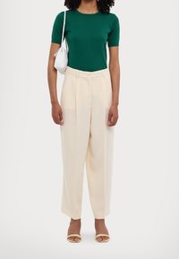 Zielony, krótkofalowy sweter, kremowe spodnie typu wide-leg i żółte sandały na otwartym palcu. Uzupełnione fakturowaną białą torebką.