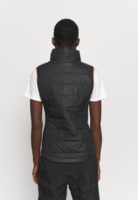 Svart ärmlös väst med hög krage, vadderad design, sidodetaljer i orange och en slät textur, bärs över en vit skjorta.