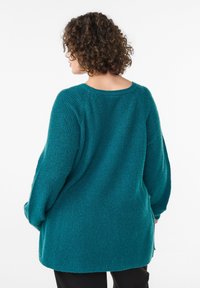 Teal oversized sweater with a textured knit, dropped shoulders, and a wide neckline. Features a straight hem and side slits for ease of movement.