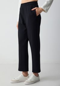 Schwarze Hosen mit elastischem Bund und Seitentaschen. Hergestellt aus einem weichen Stoff, verfügen sie über ein gerades Bein Design mit dezenten Nahtdetails.