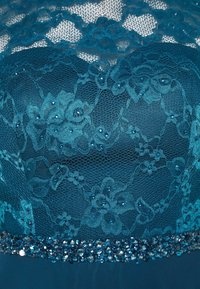 Tissu en dentelle couleur sarcelle avec motif floral superposé sur un tissu uni, orné de petites perles et d'une rangée de sequins et de pierres facettées le long du bord.