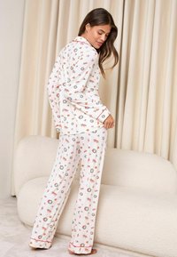 Set de pijamale albe cu model floral, cu mâneci lungi și pantaloni, cu margini roșii. Prezintă mici flori și modele de cununi în toată suprafața.
