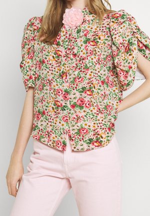 Blumenmuster Bluse mit Knöpfen und Puffärmeln, mit einem Muster in Pink, Grün und Gelb, sowie einem pinken Blumenakzent am Ausschnitt.