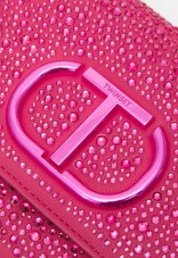 Růžový kožený povrch ozdobený různě velkými lesklými růžovými rhinestones a metalickým růžovým logem Twinset.