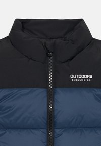 Svart och marinblå puffjacka med hög krage och frontdragkedja, med "OUTDOORS Expedition"-logotyp på bröstet.