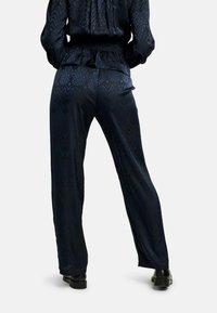 Jūras zilā satīna bikses ar teksturētu čūskādas rakstu, ar brīvu piegriezumu un elastīgu jostu, kopā ar melniem apaviem.