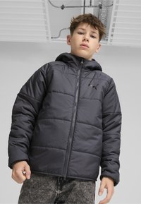Svart puffjacka med huva, dragkedjestängning, horisontell quiltning och en liten logotyp på vänster bröst. Tyget verkar slätt och hållbart.