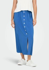 Gonna maxi blu con bottone frontale, vita elastica, spacco laterale e tessuto leggero. Abbinata a sneaker bianche per un look casual.