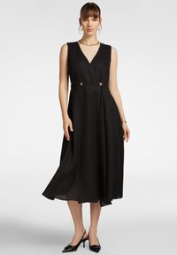 Vestito nero senza maniche con scollatura a V, design avvolgente, due bottoni decorativi in vita e gonna svasata fluida. Tessuto liscio.
