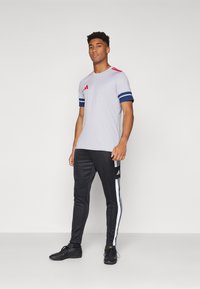 Gray athletic t-shirt with blue accents and red stripes, paired with black joggers featuring white side stripes and black sneakers.