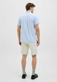 Cămașă bleu deschis cu mânecă scurtă, având guler standard, combinată cu pantaloni scurți bej, cu manșetele suflecate. Pantofi negri și șosete gri completează ținuta.