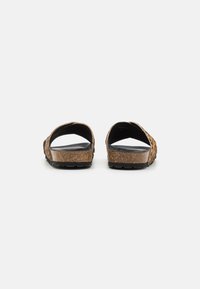 Brown woven slide sandals with open back, cork midsole, and textured rubber outsole. Soft footbed with smooth black lining.