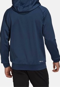 Sweat à capuche bleu marine à texture lisse, avec une coupe ajustée, des manches longues et un logo à l'ourlet inférieur.