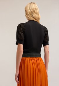 Svart topp med texturerade puffärmar, tillsammans med en flödande orange kjol med svart elastisk midja. Släta tyger och kontrasterande färger.