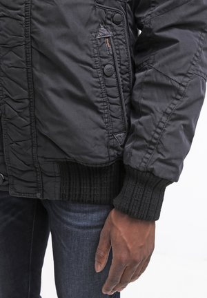 Schwarze, gesteppte Bomberjacke mit einer Reißverschlusstasche, gerippten Bündchen und einem strukturierten Saum. Verfügt über runde Knöpfe zum Verschließen und eine glatte Oberfläche.