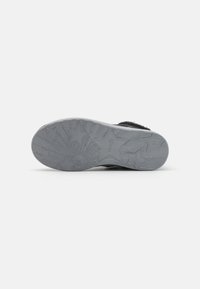 Suela de zapatilla negra con goma gris texturizada, con patrones de estrellas y estallidos de sol. Material suave alrededor del tobillo para mayor comodidad.