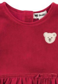 Rotes Samtkleid mit rundem Ausschnitt, das auf der linken Seite einen weißen Teddybär-Aufnäher und einen Rüschensaum zeigt.