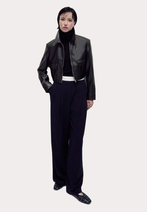Black leather cropped jacket with high collar, paired with navy high-waisted trousers and black flats featuring silver studs.