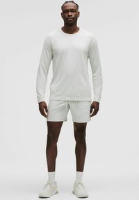 Helles Sportoutfit mit einem langärmeligen Oberteil und Shorts. Der Stoff hat eine glatte Textur mit subtiler Rippung an den Ärmeln.