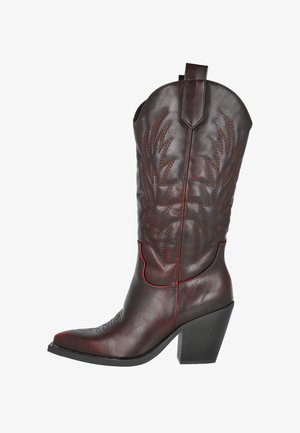 Bota de cowboys de cuero marrón oscuro con costuras decorativas, puntera afilada y tacón apilado.