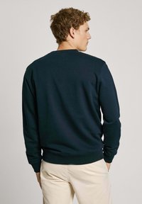 Sudadera azul marino con cuello redondo y mangas largas, hecha de una tela suave. Presenta puños y dobladillo acanalados, vista desde la parte posterior.