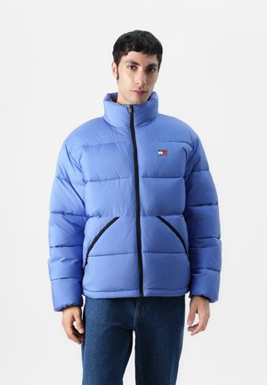 Giacca trapuntata azzurra chiara con collo alto, zip frontale e dettagli neri a contrasto; presenta un design a trapuntatura e una patch con logo.