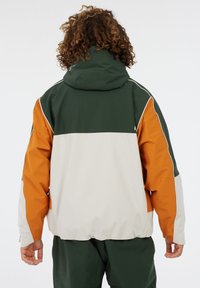 Kleurblokjasje met een groene bovenkant, oranje mouw en een crèmekleurig onderste gedeelte. Gemaakt van glad, waterafstotend materiaal. Verstelbare capuchon.