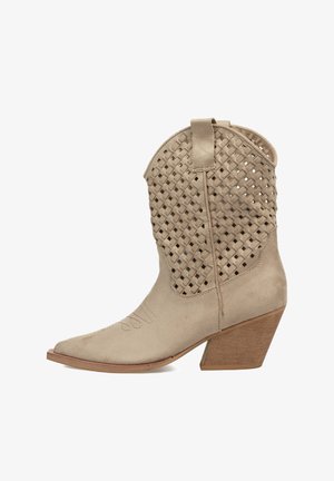 Botín de ante beige con parte superior trenzada, punta afilada y tacón de madera apilada. Cuenta con una lengüeta para facilitar el uso.