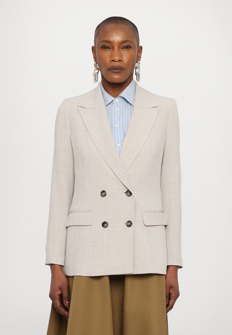 Lys beige dobbeltspent blazer laget av teksturert stoff, med store svarte knapper og normal krage, kombinert med en lyseblå stripete skjorte.