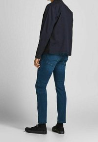 Navy cotton jacket with buttoned cuffs, paired with fitted blue denim jeans. Black sneakers complete the outfit. Simple, casual design.