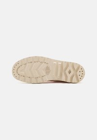 Suela de zapato de goma beige, con una superficie texturizada que presenta surcos profundos y un patrón para mayor tracción. Detalle del logo notable en el centro.