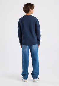 Tummansininen collegepaita, jossa on ribbireunat hihansuissa ja helmassa, yhdistettyinä löysiin vaaleansinisiin farkkuihin. Yksinkertainen, rento muotoilu.