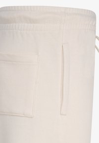 Beige Baumwolltasche mit Zugverschluss, ausgestattet mit einer Seitentasche und strukturiertem Stoff. Einfaches Design mit praktischen Akzenten.