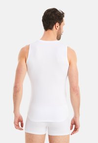 White cotton tank top with a fitted design, featuring wide straps and a smooth texture. Worn with matching white shorts.
