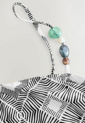 Sangle en tissu à motifs noir et blanc avec un accent de perles décoratives en vert, blanc, bleu et marron, présentant des textures lisses et mates.