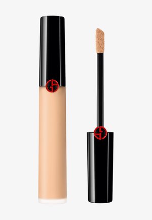Flytende foundation i en gjennomsiktig beige flaske med en blank svart kork, med en rød logo. Inkluderer en myk applikatorstang.