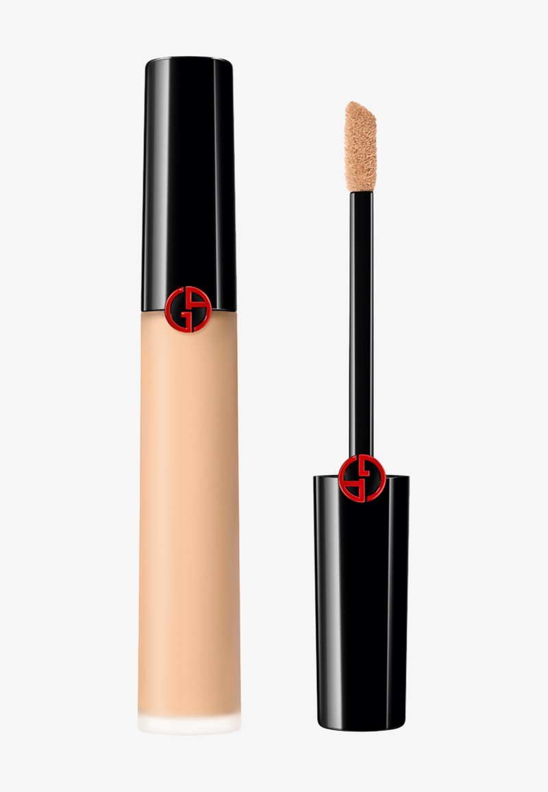 Base líquida en un frasco transparente beige con una tapa negra brillante, que presenta un logo rojo. Incluye un aplicador suave.