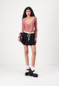 Red and white checkered cropped top with long sleeves and tie detail, paired with a black pleated mini skirt and chunky black platform shoes.