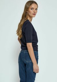 Námořnický svetr s krátkým rukávem, s těsným střihem, ribbed texturou a kulatým výstřihem. Spárovaný s tmavě modrými džíny se standardními kapsami.