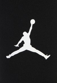 Zwarte stof met een prominent wit silhouet van een springende figuur die een basketbal vasthoudt, met een ribbelstructuur.