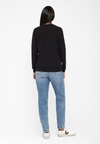 Zwarte sweatshirt met ronde hals, lange mouwen en ribgebreide manchetten, gecombineerd met lichtblauwe rechte jeans en witte sneakers.