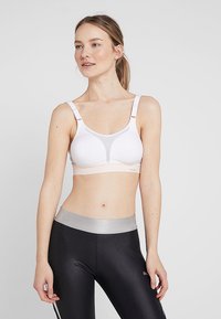 Sport-bh i hvitt og lys rosa med mesh-detaljer, justerbare stropper og et bredt grått bånd. Kombinert med svarte leggings med reflekterende midjebånd.