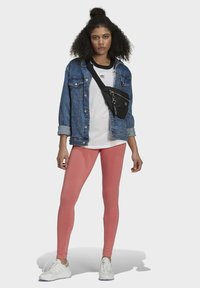 Jeansowa kurtka, biała koszulka z logo, różowe legginsy i białe buty sportowe, z czarną torebką na ramię z detalem w postaci zamka.