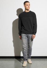 Dunkelgrauer strukturierter Pullover mit einem gerippten Muster an den Schultern, kombiniert mit hellgrauen Jeans und beige-farbenen Sneakern.